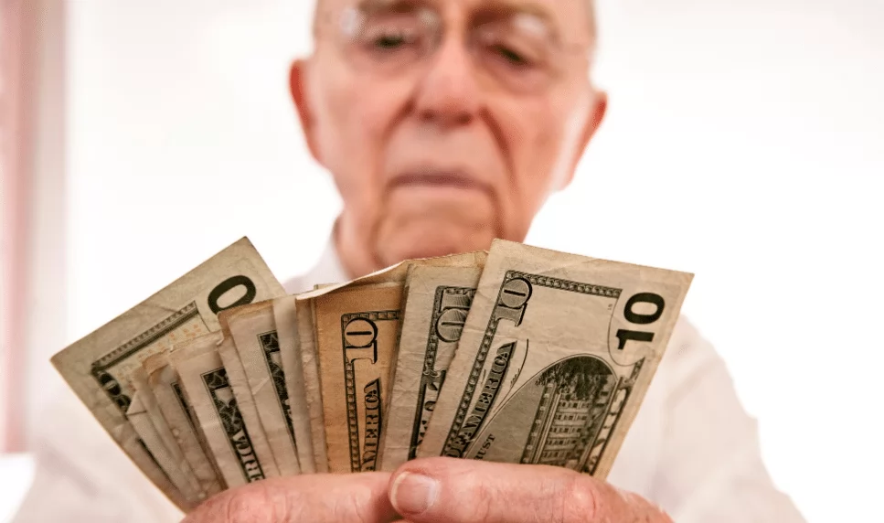 senior man holding several 10 and 1 dollar bills in hands learning how to save money