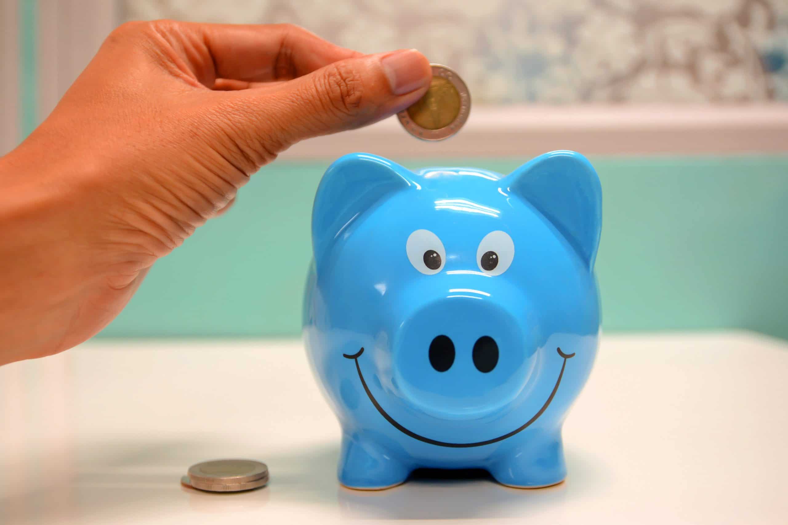 person putting a coin into a blue piggy bank for frugal retirement living